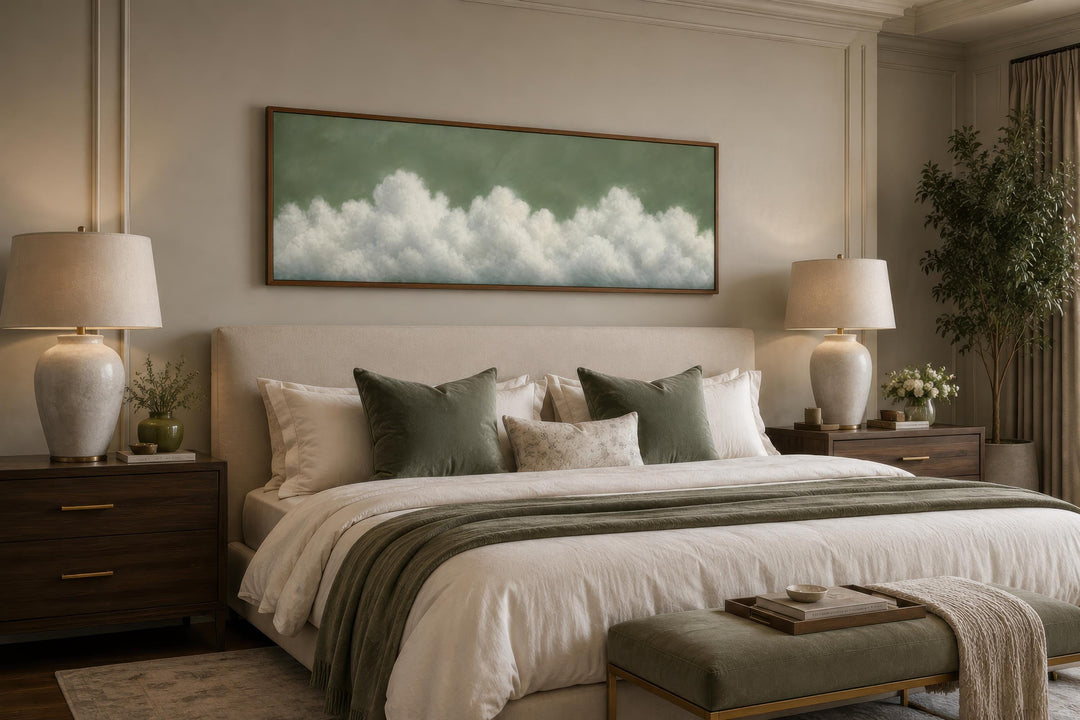 Long narrow sage green canvas wall art with soft white clouds hanging above a bed in a bedroom.