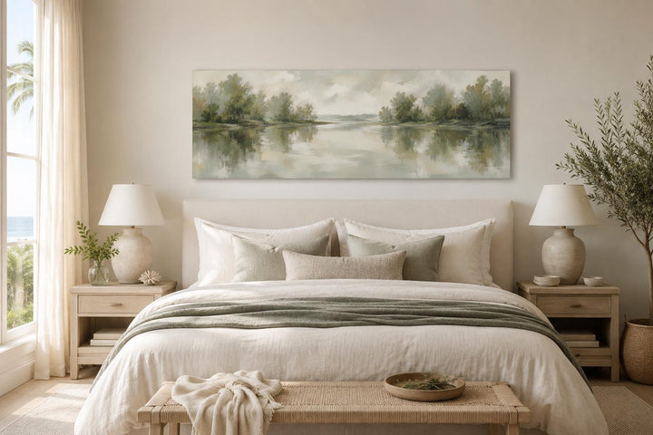 Sage green lake reflection landscape canvas print hanging above a bed in a neutral bedroom.