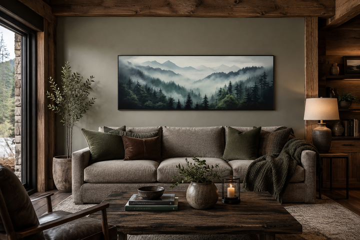 Sage green foggy pine forest and mountains landscape wall art in a black frame above a sofa.