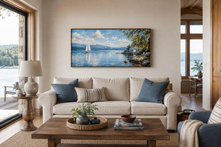 Sailboat in mountain lake canvas print hanging above a beige sofa in a coastal living room.