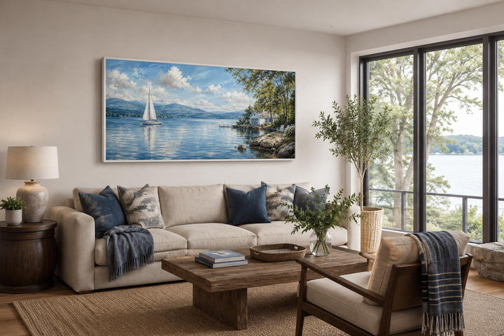 Sailboat in mountain lake painting on a canvas print hanging above a beige sofa in a living room.