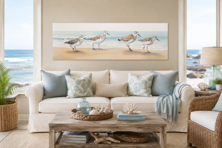 Panoramic framed canvas wall art of four sandpipers walking on a sandy beach by the ocean.