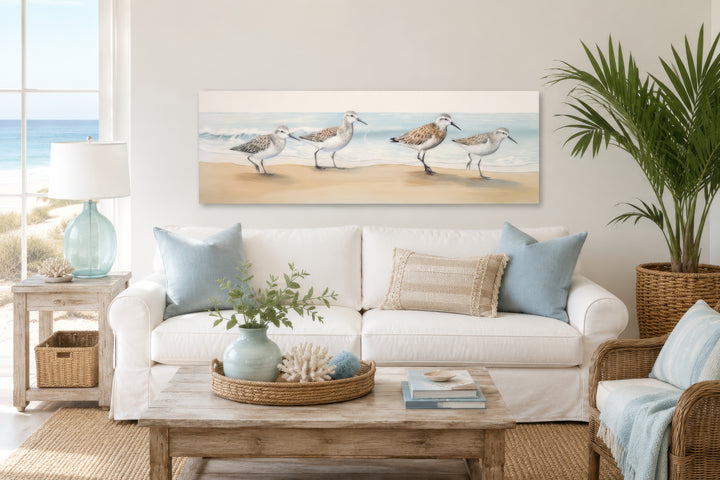 Panoramic framed canvas wall art of four sandpipers walking on a sandy beach by the ocean.