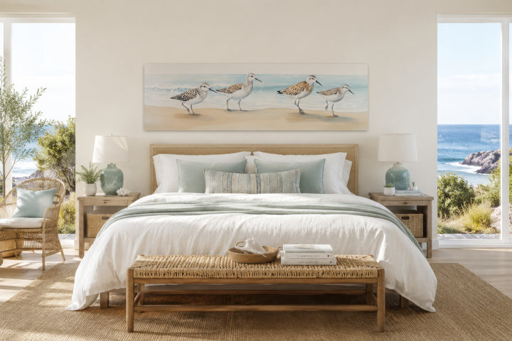 Horizontal framed canvas wall art of four sandpipers walking on a sandy beach by the ocean.