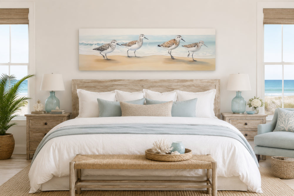 Sandpipers walking on the beach horizontal framed canvas wall art above a bed in a coastal bedroom.