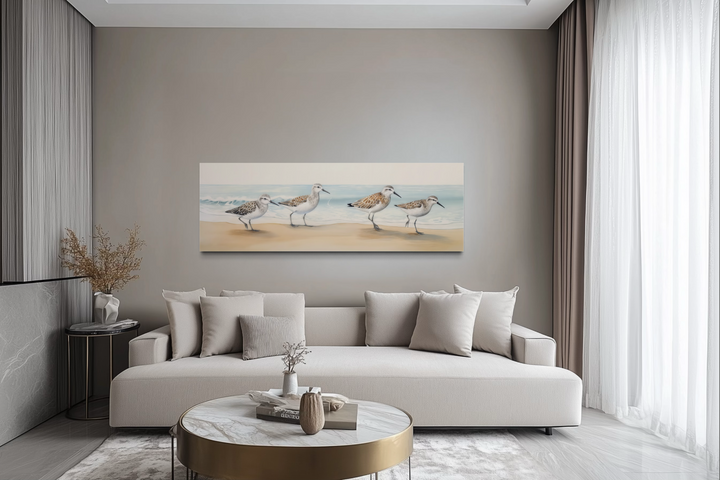 Sandpipers walking on the beach horizontal framed canvas wall art above a modern beige sofa.