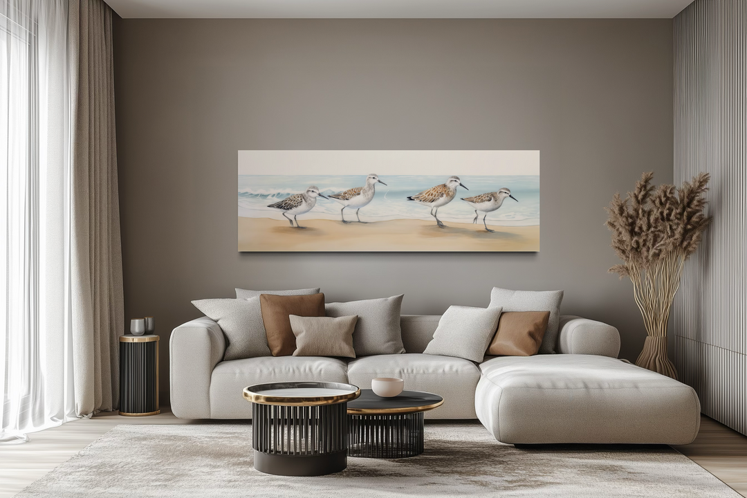 Horizontal framed canvas wall art of four sandpipers walking on a beach above a modern sofa.