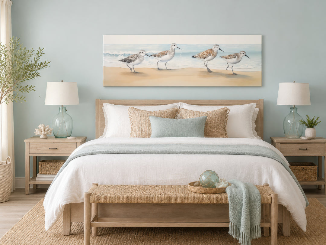 Panoramic framed canvas wall art of four sandpipers walking on a sandy beach above a bed.