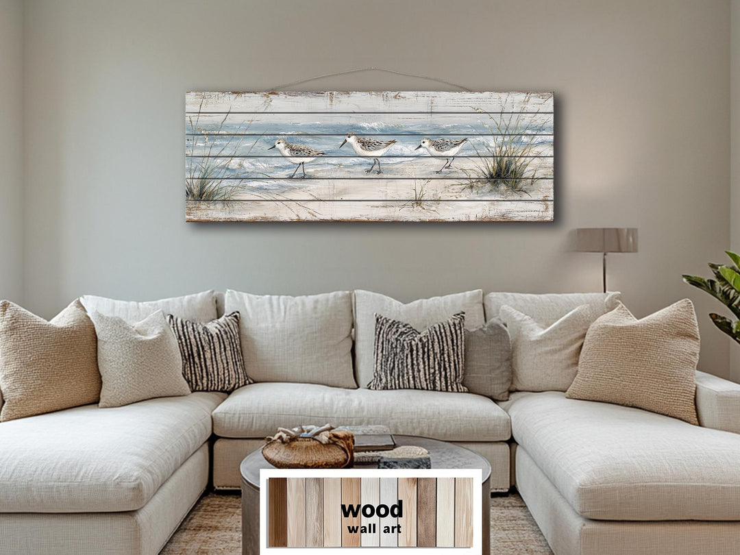 Long narrow wood wall art featuring three sandpipers on a beach, hanging above a neutral sofa.