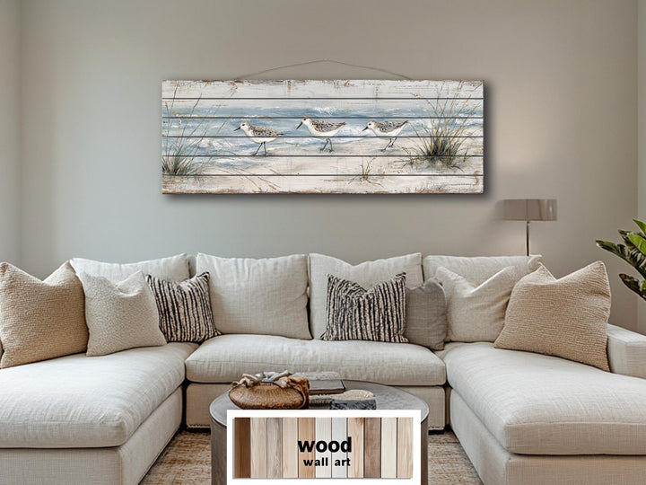 Long narrow wood wall art featuring three sandpipers on a beach, hanging above a neutral sofa.