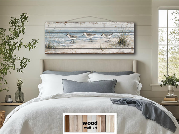Long narrow wood wall art featuring three sandpipers on a beach, hanging above a bed.