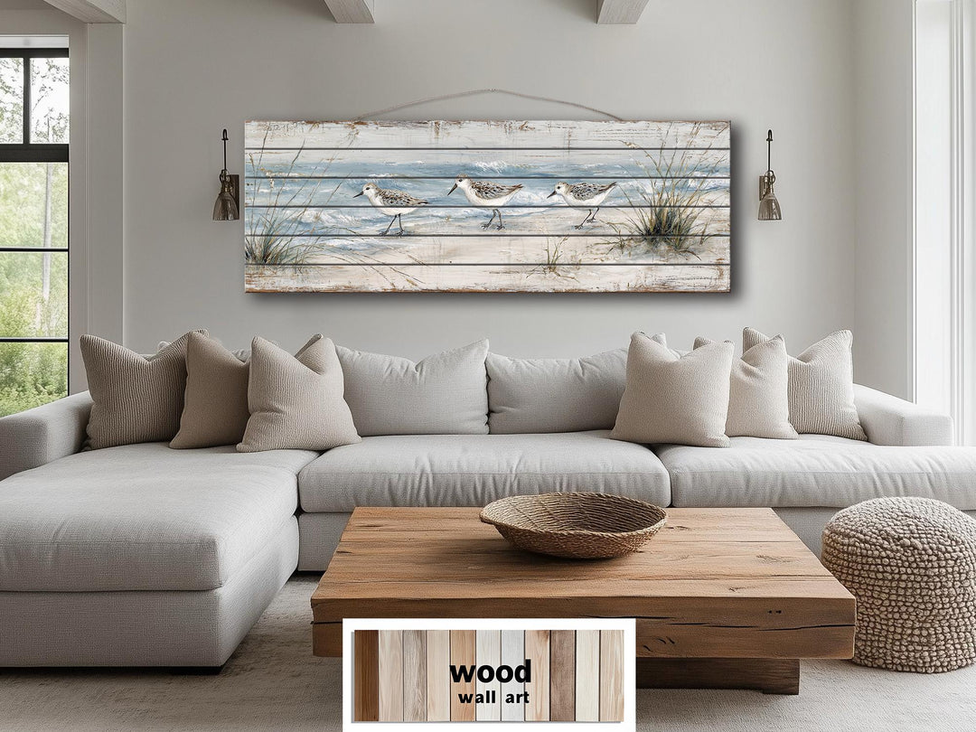 Long narrow wood wall art featuring three sandpipers on a beach, hanging above a sofa.