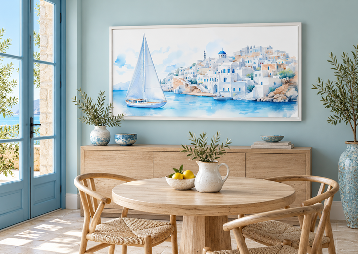 Santorini Sea and Sailboat Framed Canvas Wall Art in a white frame above a wooden sideboard.