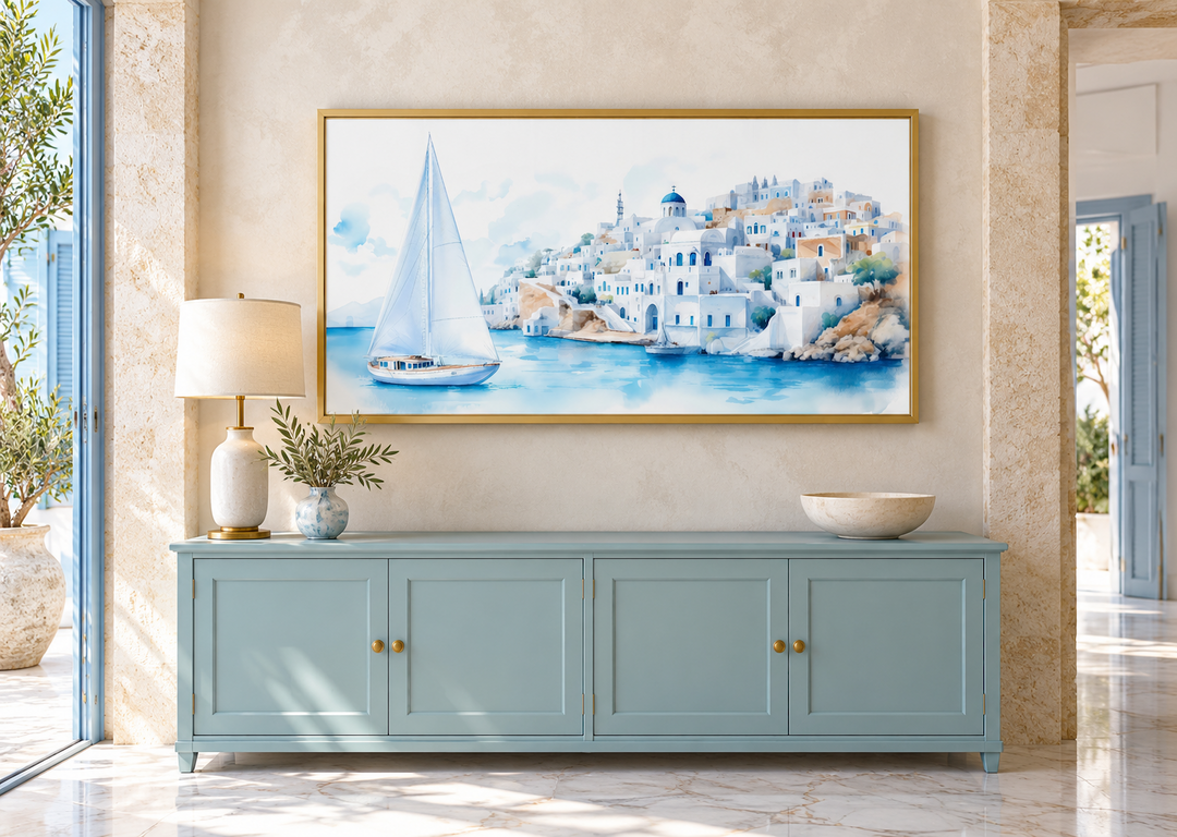 Santorini Sea and Sailboat Framed Canvas Wall Art in a gold frame above a blue sideboard.