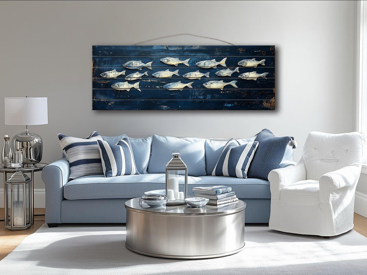 Long narrow distressed wood wall art featuring a school of fish over a blue sofa in a coastal room.