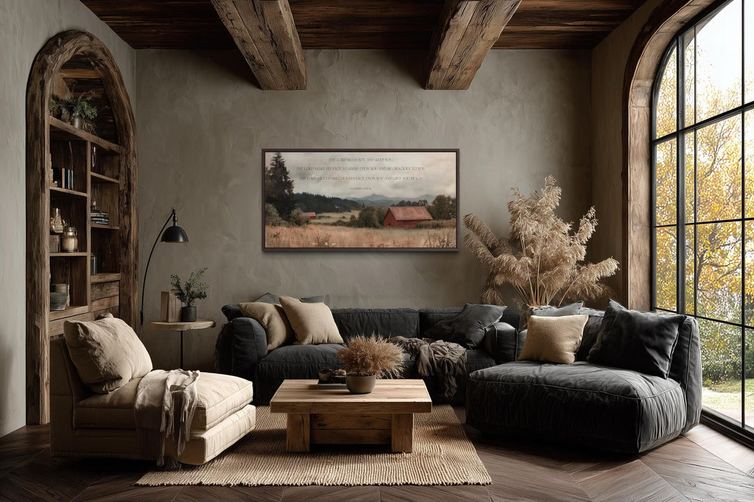 A framed landscape painting with a red barn and Numbers 6:24-26 scripture hangs in a rustic room.