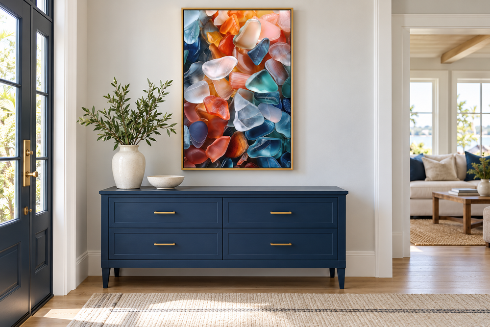 Vertical sea glass abstract painting in a gold frame above a navy blue dresser in a coastal home.