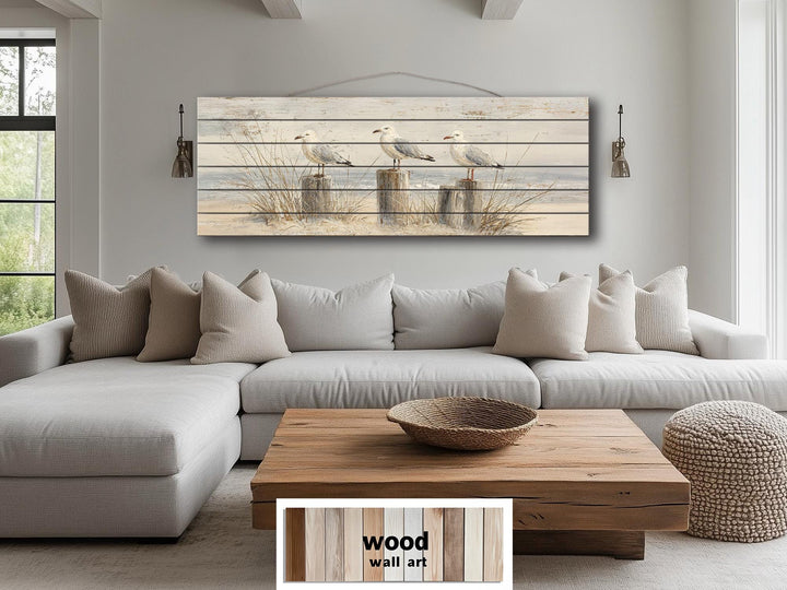 Large horizontal wood wall art featuring three seagulls on beach posts above a neutral sofa.
