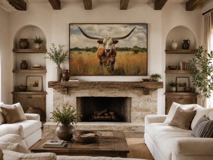 Framed canvas wall art of a Texas Longhorn cow in a field above a rustic stone fireplace.
