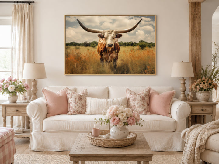 Texas Longhorn cow in a field framed canvas wall art hanging above a white sofa in a living room.