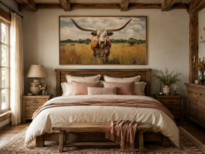 Framed canvas wall art of a Texas Longhorn cow in a field hung above a rustic wooden bed.