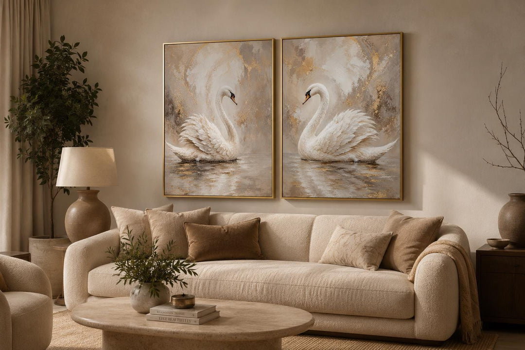 Set of two white swan canvas art prints with gold accents hanging above a cream sofa.