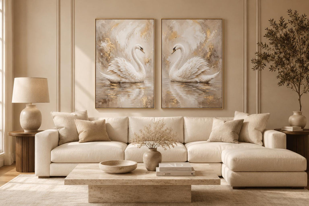 Set of 2 white swan canvas art prints with gold accents above a cream sofa in a glam living room.