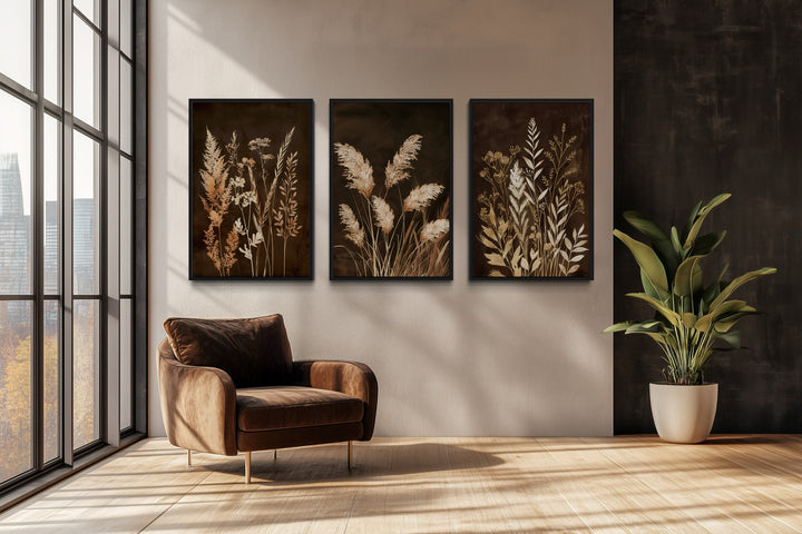 Set of 3 brown and beige boho botanical grass canvas prints on a wall above a brown velvet chair.