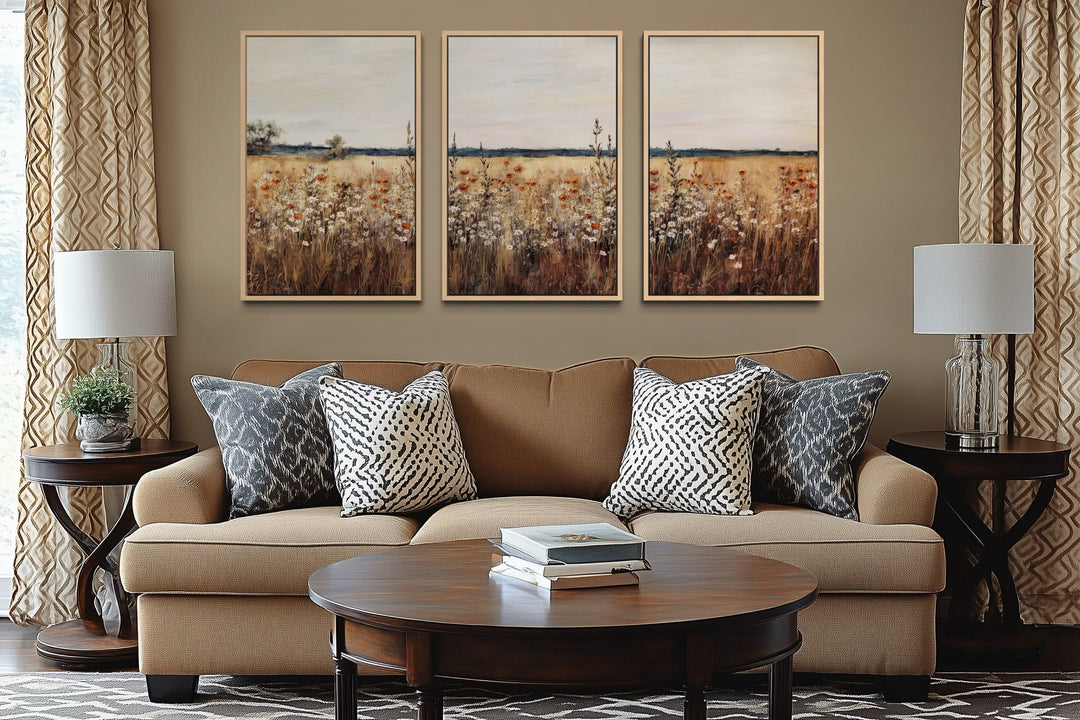 Set of 3 framed canvas wildflower field paintings hanging above a brown sofa in a farmhouse room.