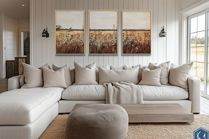 Set of 3 framed canvas prints featuring a rustic wildflower field above a neutral sectional sofa.