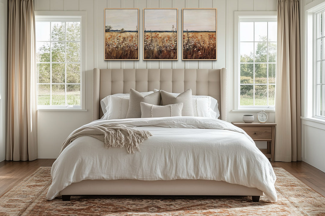 Set of 3 rustic wildflower field framed canvas wall art panels hanging above a neutral tufted bed.