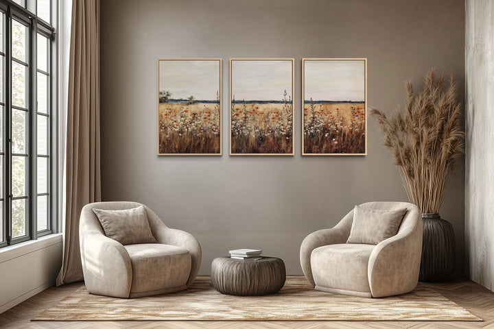 Set of 3 rustic wildflower field framed canvas prints above two beige armchairs in a neutral room.