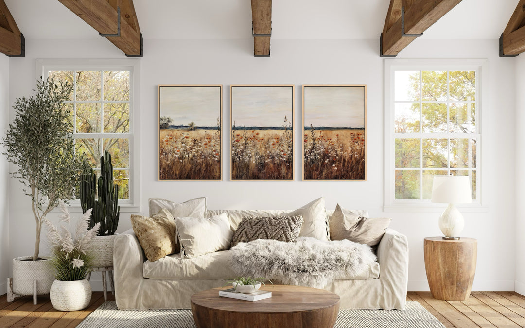 Set of 3 rustic wildflower field framed canvas wall art panels above a sofa in a farmhouse room.