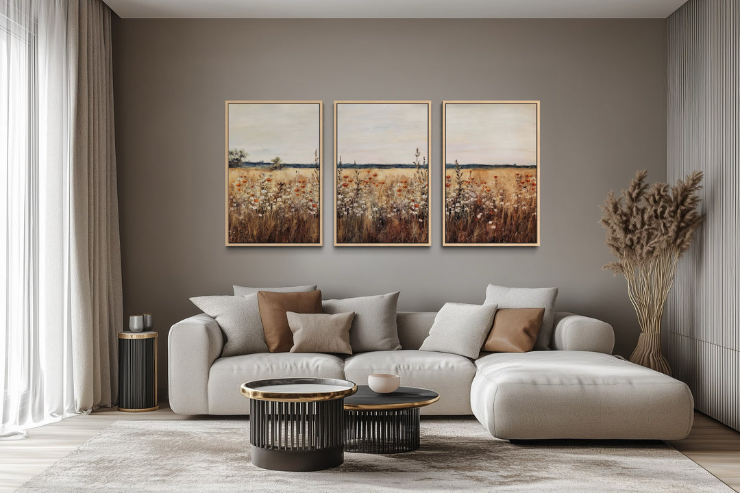 Set of 3 rustic wildflower field framed canvas wall art panels above a modern sofa in a living room.