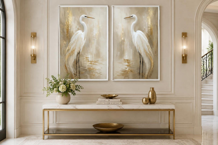 Set of two canvas wall art pieces featuring white egrets in golden water above a console table.