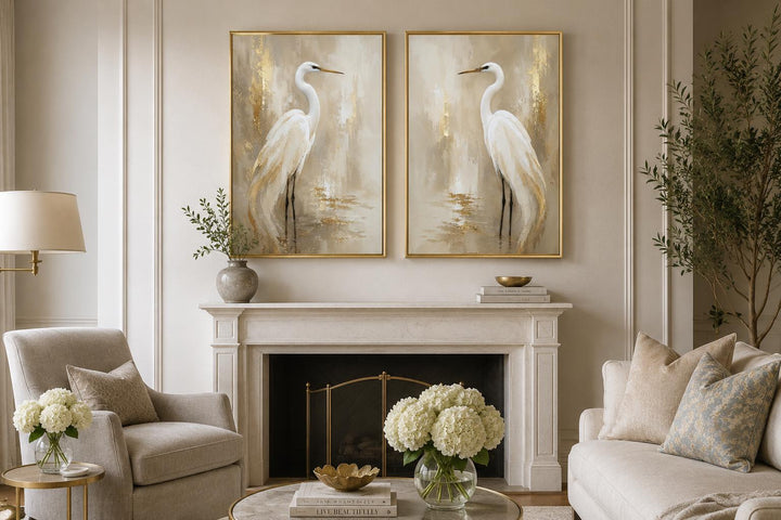 Set of 2 white egret canvas wall art with gold accents hung above a fireplace in a neutral room.