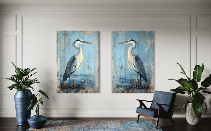Set of 2 rustic blue heron paintings on weathered wood-textured canvas in a coastal living room.