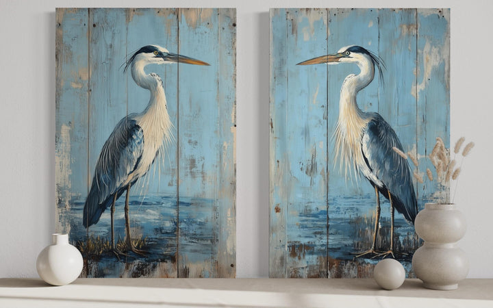 Set of two rustic blue heron paintings on vertical wood-textured canvas with a distressed finish.