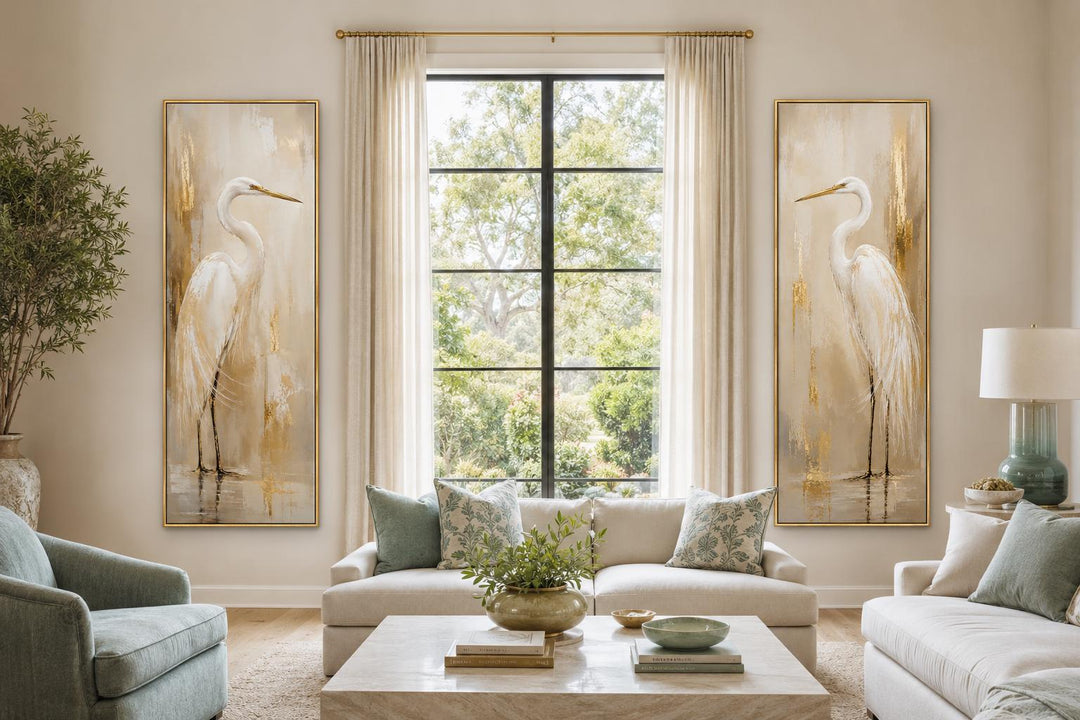 Set of 2 tall narrow white egret canvas prints with gold accents flanking a window in a living room.
