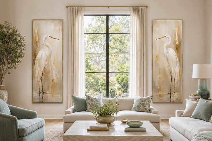 Set of 2 tall narrow white egret canvas prints with gold accents flanking a window in a living room.
