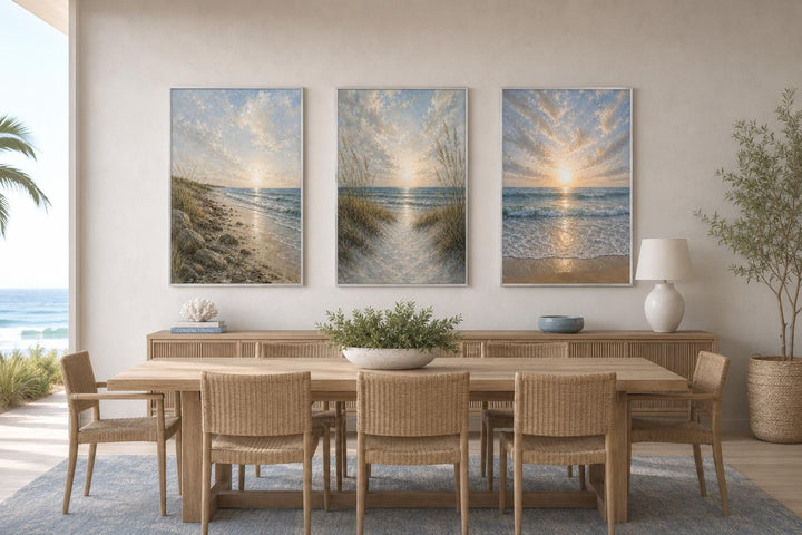 Set of 3 vertical beach sunset canvas prints above a wooden dining table in a coastal room.