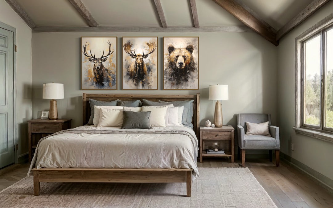 Set of 3 framed wildlife canvas prints featuring a bear, moose, and elk above a bed in a cabin.