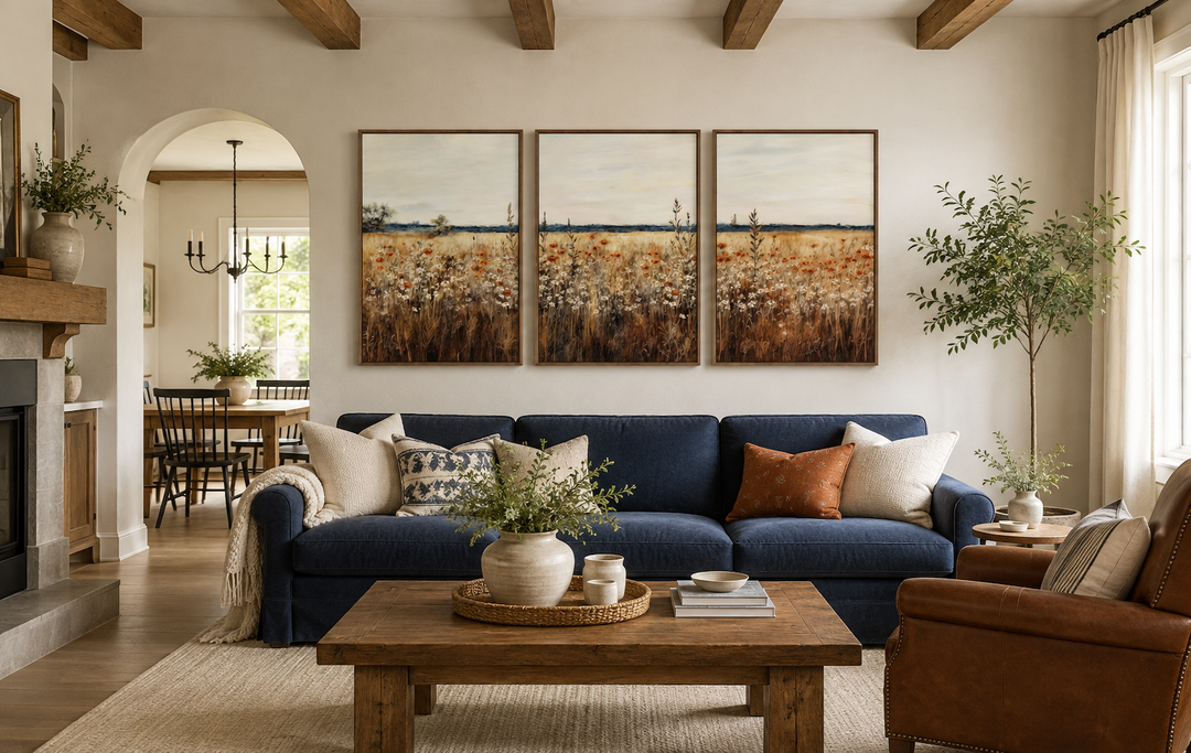 Set of three framed canvas prints featuring a rustic wildflower field above a navy blue sofa.