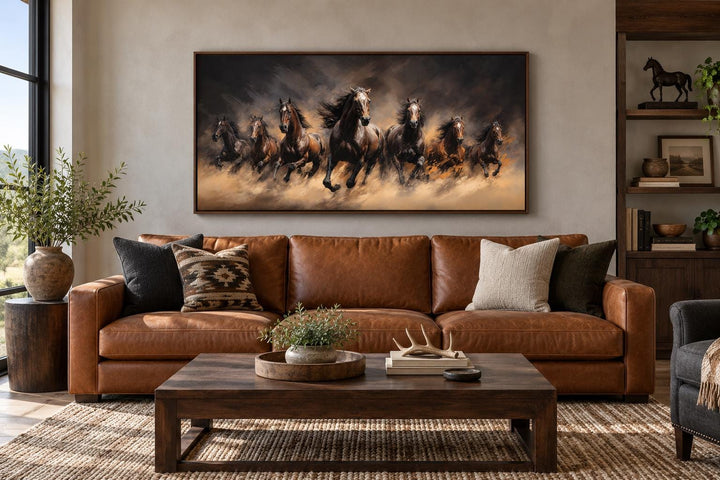 Seven wild horses galloping through swirling dust framed canvas wall art above a leather sofa.