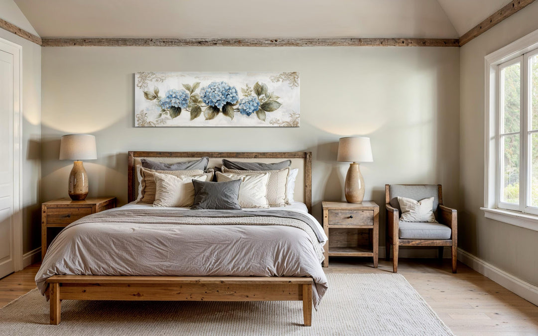 Long horizontal canvas wall art of blue hydrangeas hanging above a bed in a rustic bedroom.