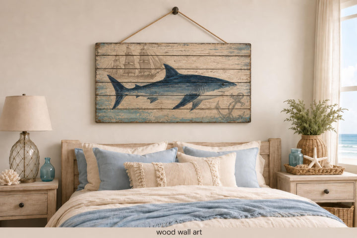 Distressed wood panel wall art featuring a blue shark, vintage ship, and anchor in a coastal bedroom.