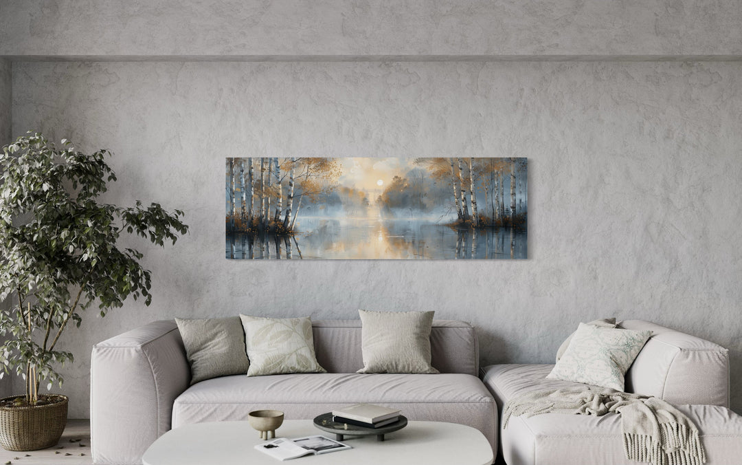 Panoramic wall art of a misty silver birch forest over a lake, hung above a modern sofa.