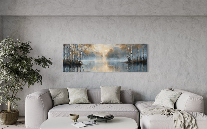 Panoramic wall art of a misty silver birch forest over a lake, hung above a modern sofa.