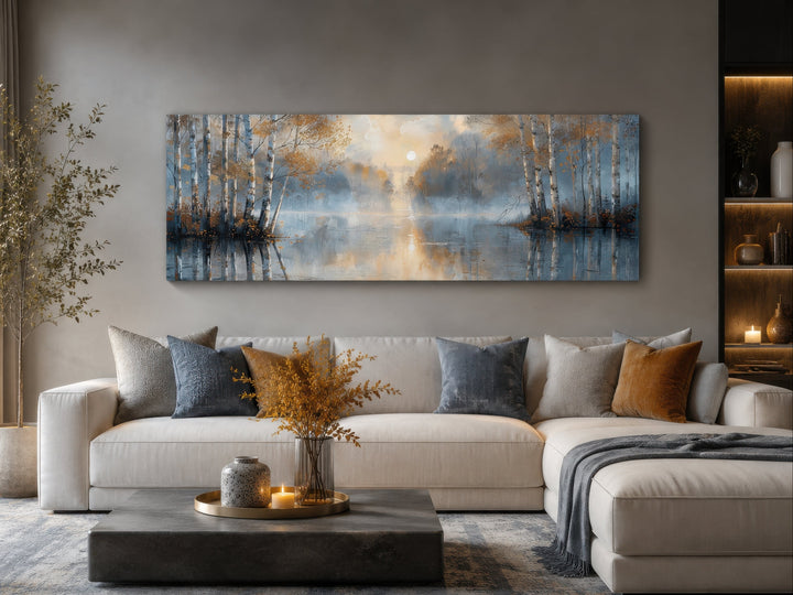 Panoramic wall art of a misty silver birch forest over a lake, hung above a modern sectional sofa.