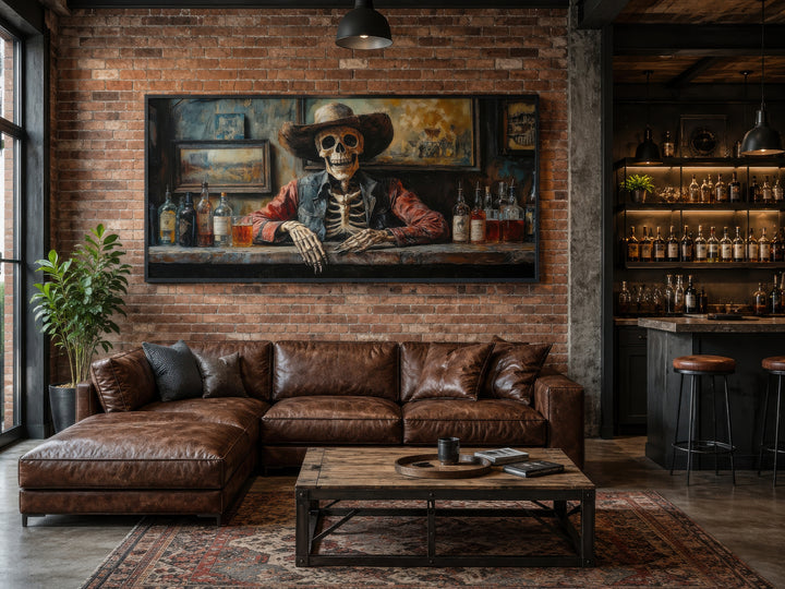 Framed canvas wall art of a skeleton cowboy barman in a saloon above a brown leather sectional sofa.
